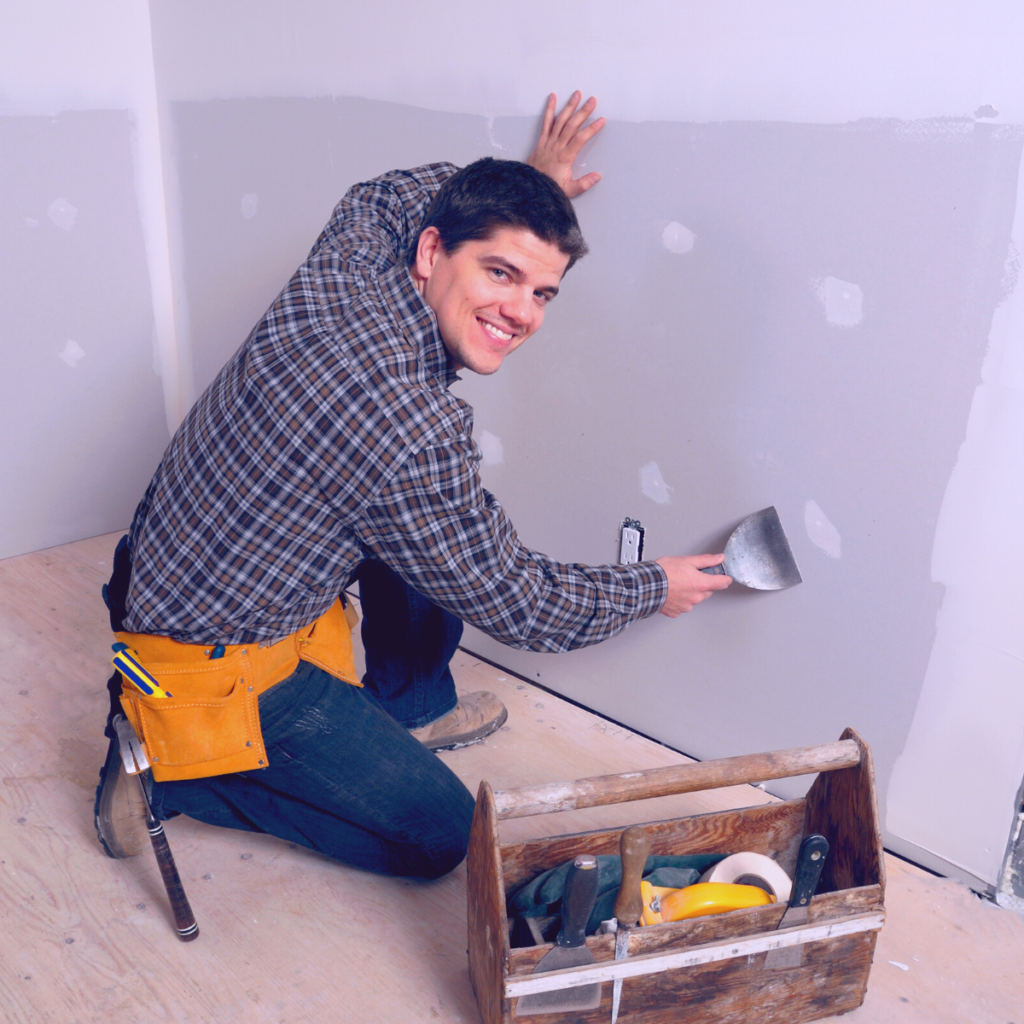 homme répare un mur avec de l'enduit et une spatule il a une boîte à outils pour faire des travaux